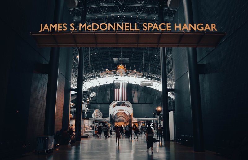 Interior view of the James S. McDonnell Space Hangar featuring a showcased spacecraft with visitors exploring.