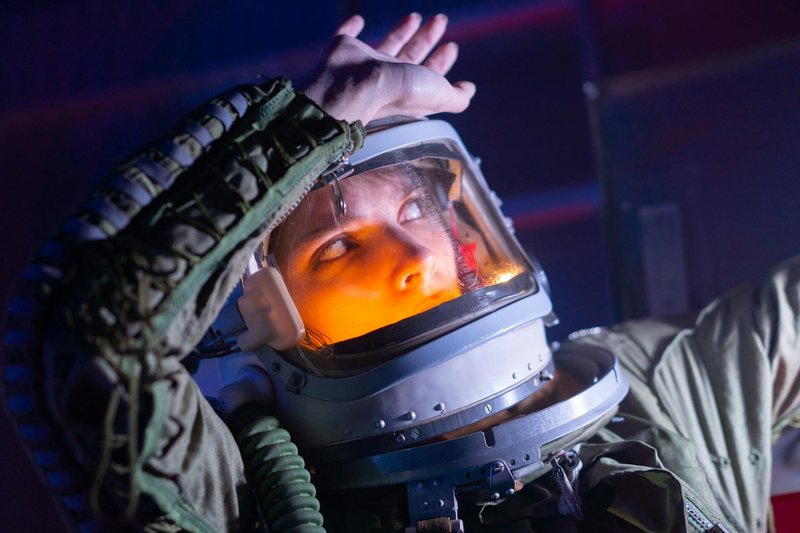Female astronaut in a space suit looks upwards, illuminated in a futuristic setting.