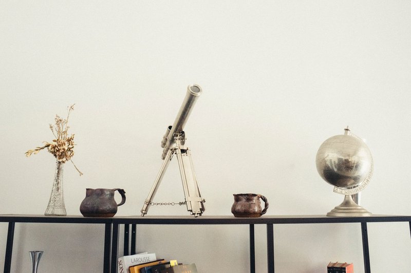 A modern shelf displaying a telescope, globe, books, and vases for a classy decor.