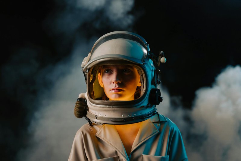 A close-up shot of a female astronaut in a helmet surrounded by smoke and neon light.