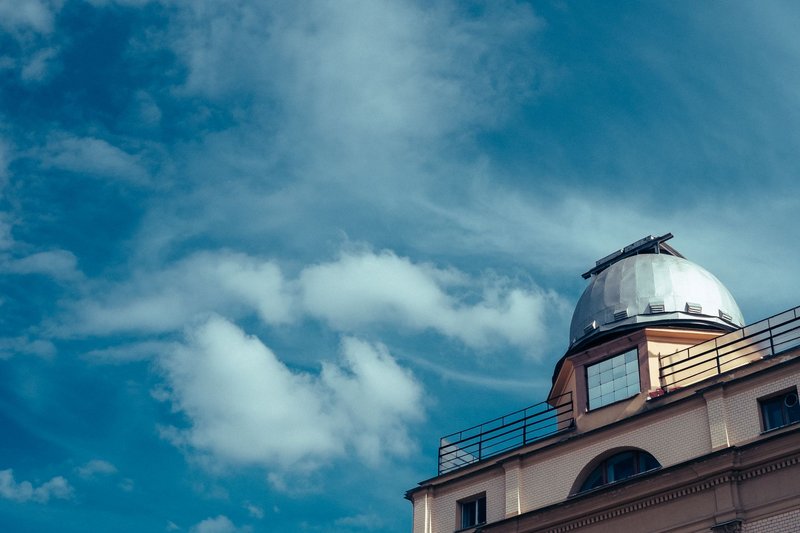 Low angle view of an observatory dome against a bright blue sky with clouds.
