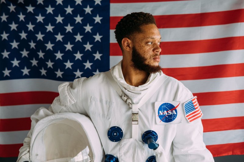 Portrait of a man in a space suit against an American flag backdrop, representing NASA.