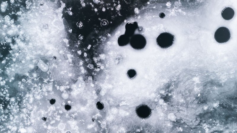 Close-up of a textured frozen ice surface with black circular formations creating abstract patterns.