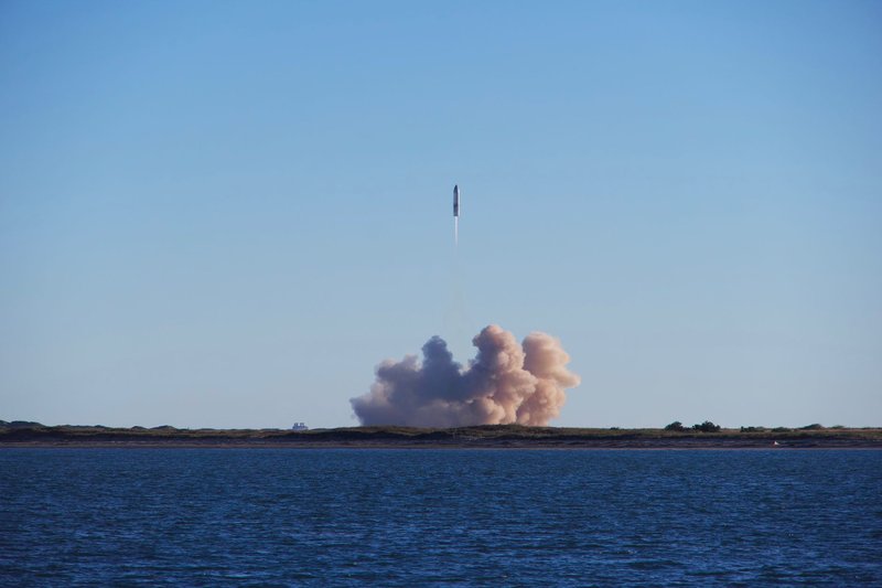 A rocket launch with smoke trails over South Padre Island, viewed across the ocean.
