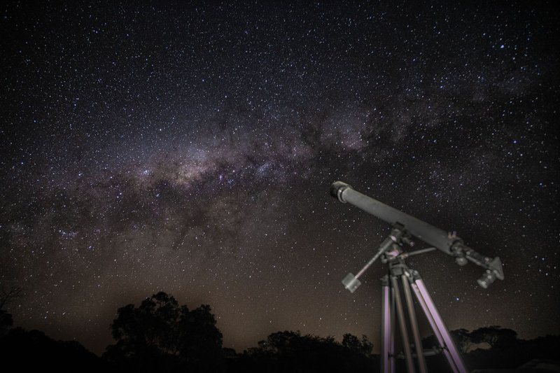 A telescope gazes at a stunning starry night sky showcasing the Milky Way.