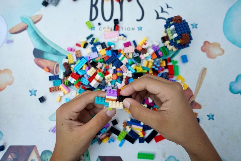 Hands of a child assembling colorful Lego bricks on an outdoor table, showcasing creativity and playfulness.
