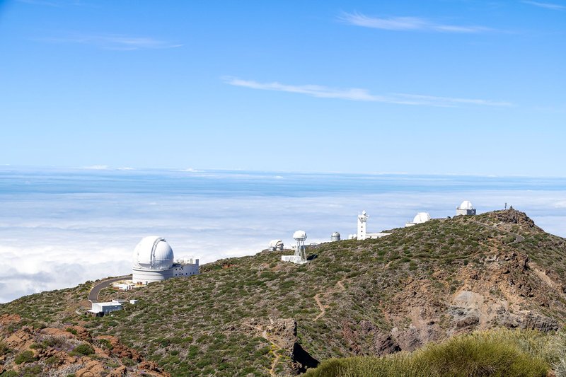 Scenic view of observatory on La Palma hilltop with clear blue skies and clouds below.