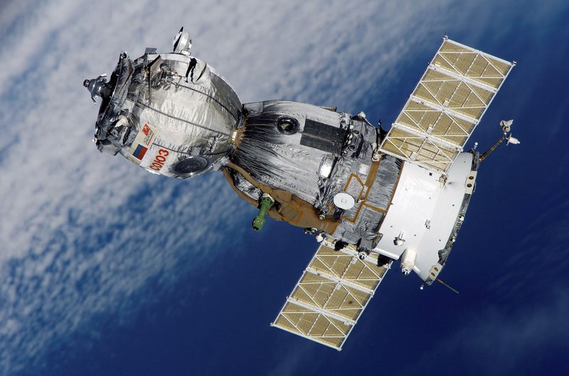 Close-up of Soyuz spacecraft orbiting Earth with solar panels extended, showcasing space exploration technology.